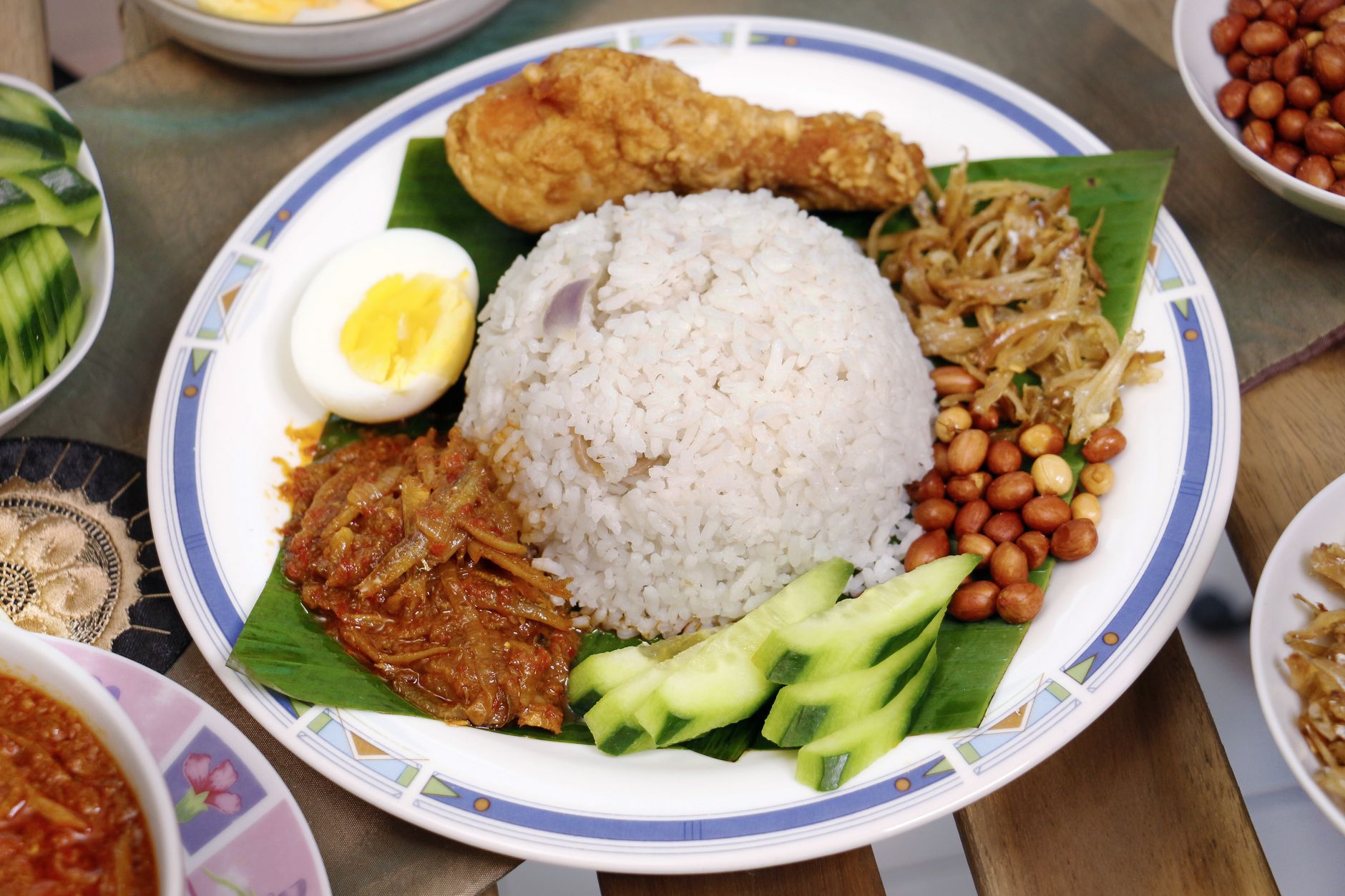 Plate of nasi lemak with fried chicken, egg, peanuts, anchovies and sambal on a banana leaf
