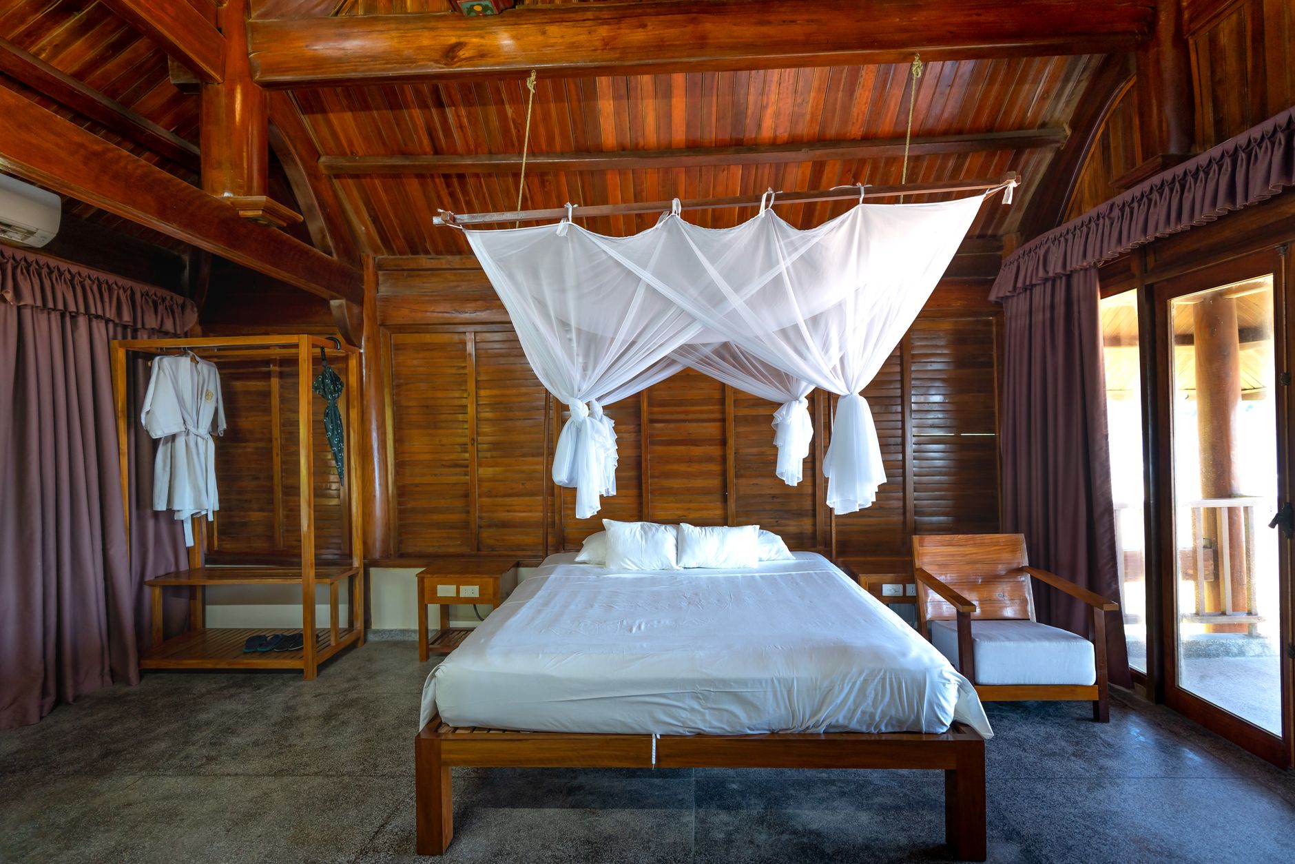 Timber guest room with a white canopy bed and shuttered walls